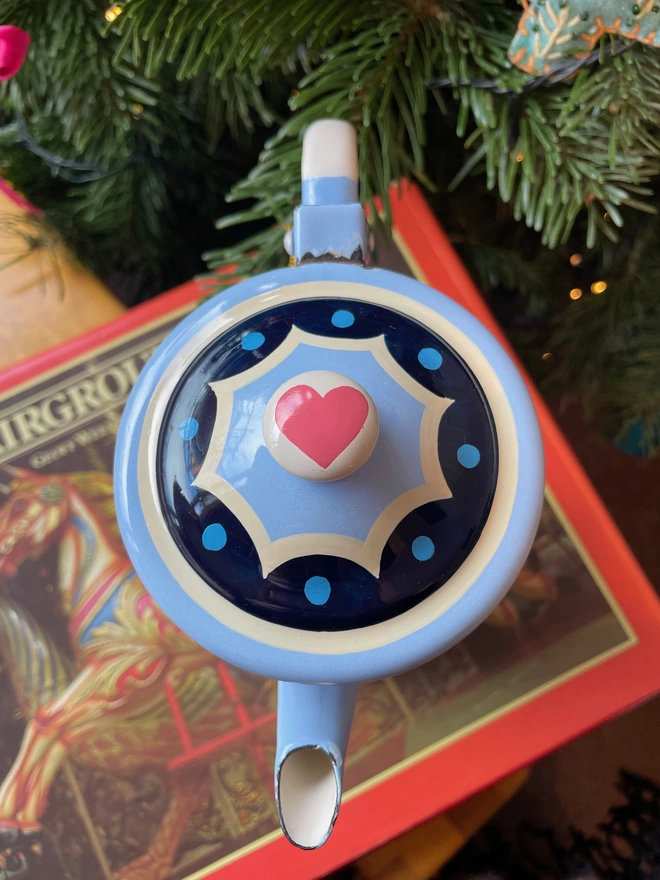 Lid of enamel coffee pot shows blue scallop edge and a pink heart