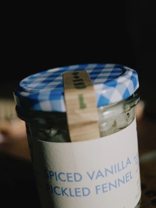 Jar Of Spiced Vanilla Pickled Fennel, jar of sauce with a blue lid on a table. 