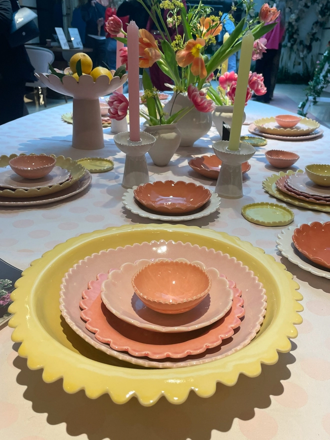 tablesetting with serving bowls, plates, candlestick holders. Scalloped edges on coloured tableware.