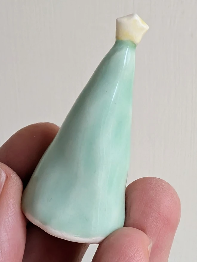 green miniature ceramic christmas tree cake topper held in fingers