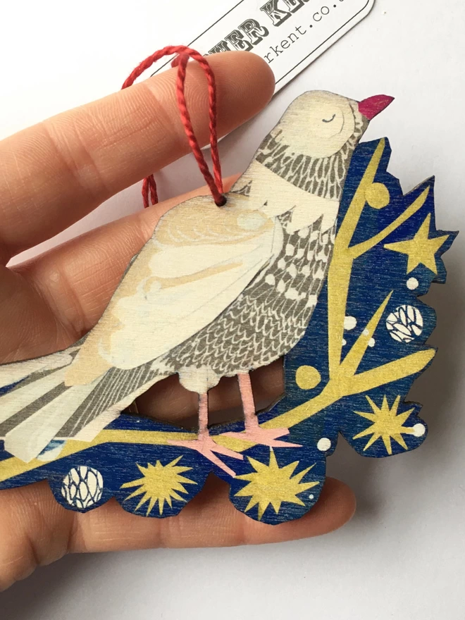 Illustrated peace dove standing on a gold star-spangled twig on a blue backroung. The cut-out decoration rests in a hand