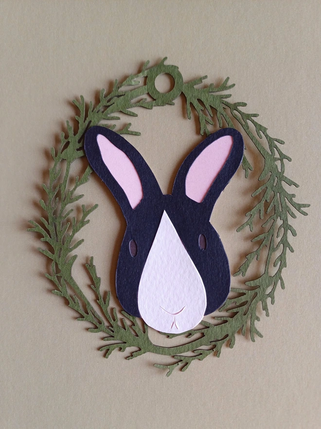 Black Bunny Easter Tree Decoration. Black bunny face with white nose patch, brown eyes and pale pink ears inside olive green foliage wreath oval