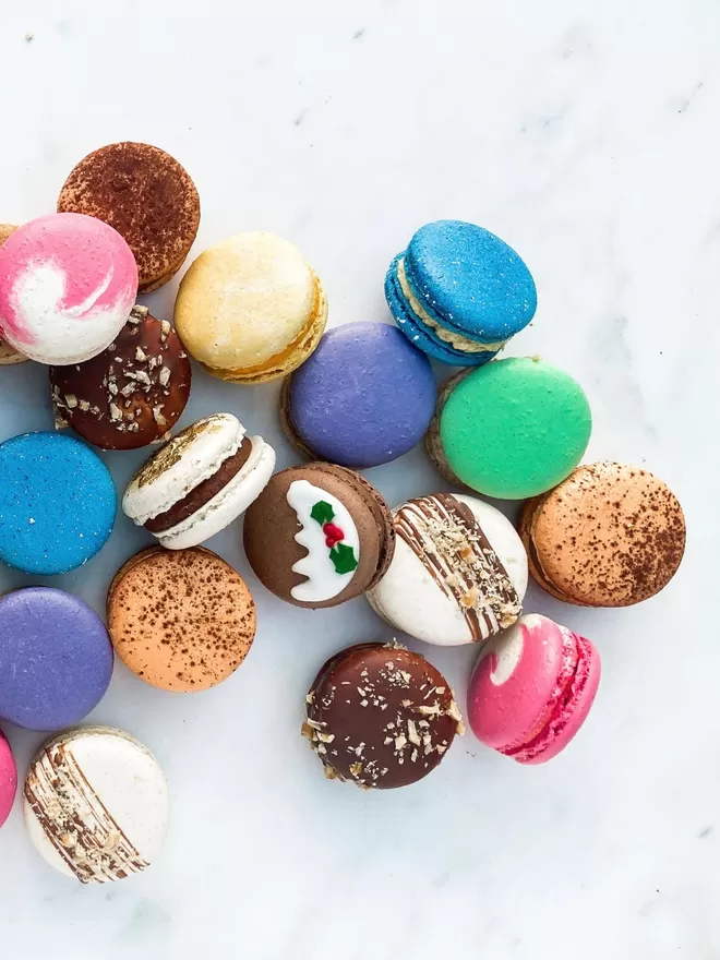 many different coloured Christmas macarons on a white marble surface