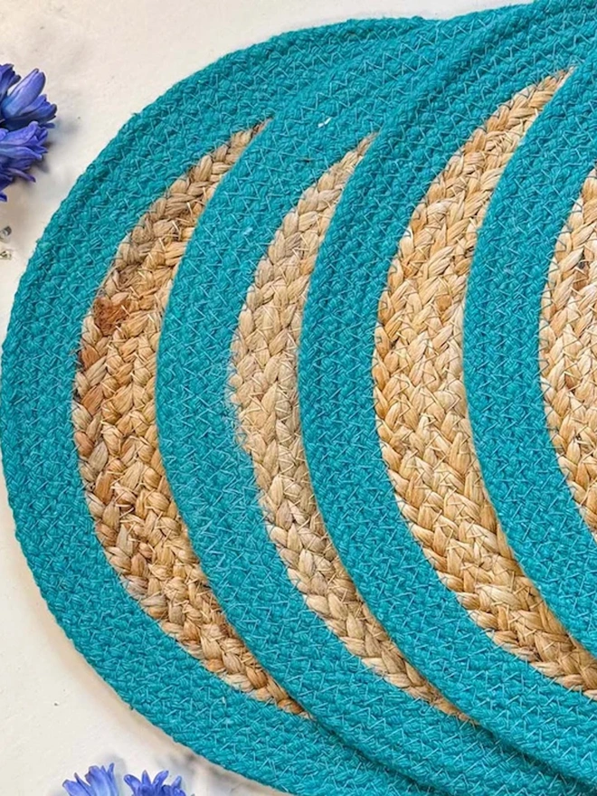 Close up of a round woven seagrass placemats with teal rings, shown on a light surface. 