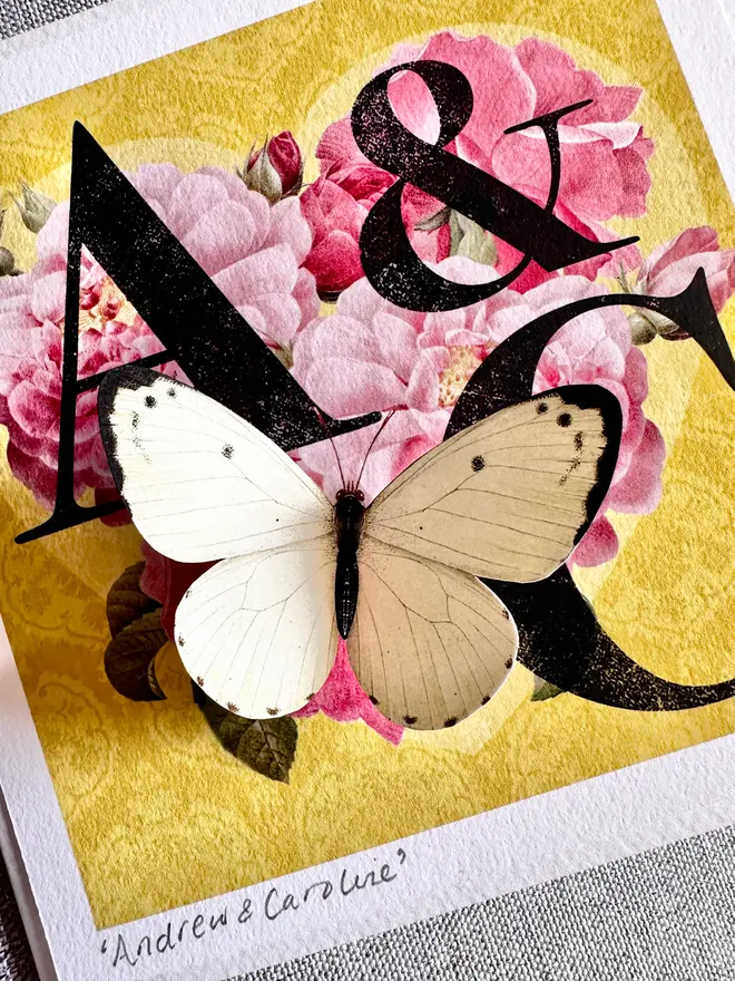 A close up of a white paper cut three dimensional butterfly sitting on a floral, rose, heart.  The couple's names are hand written and signed on the bottom left hand corner with pencil.