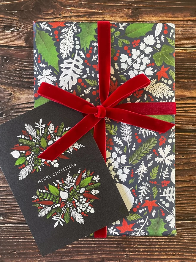 Christmas Card Resting on Gift Wrapped in Coordinating Pressed Winter Leaf Design with Red Velvet Bow
