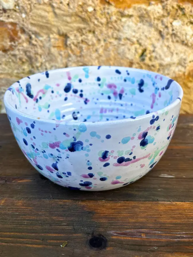 Sweetpea Ramen Bowl, a colourful ramen bowl sat on a wooden surface in front of a brick backdrop. 