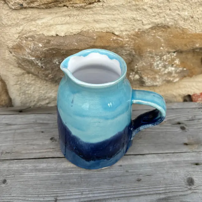 Landscape Medium Jug, a colourful jug sitting on a wooden surface against a brick backdrop. 