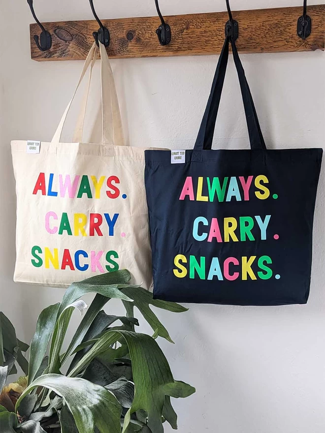 Two hanging canvas tote bag with Always Carry Snacks slogan