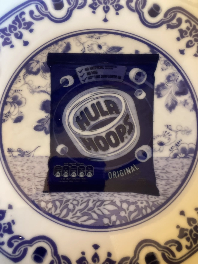 Blue and white Delft style decorative plate featuring a packet of Hula Hoops crisps in the centre.