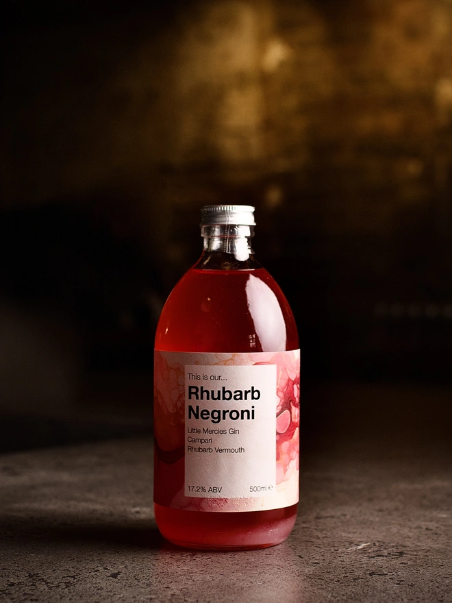 A bottle of Rhubarb Negroni shown against a moody interior background