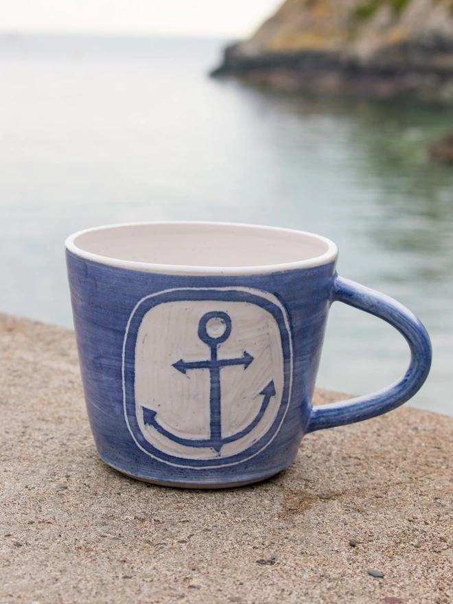 Blue mug with anchor design scratched into the clay surface, sitting on the harbour wall