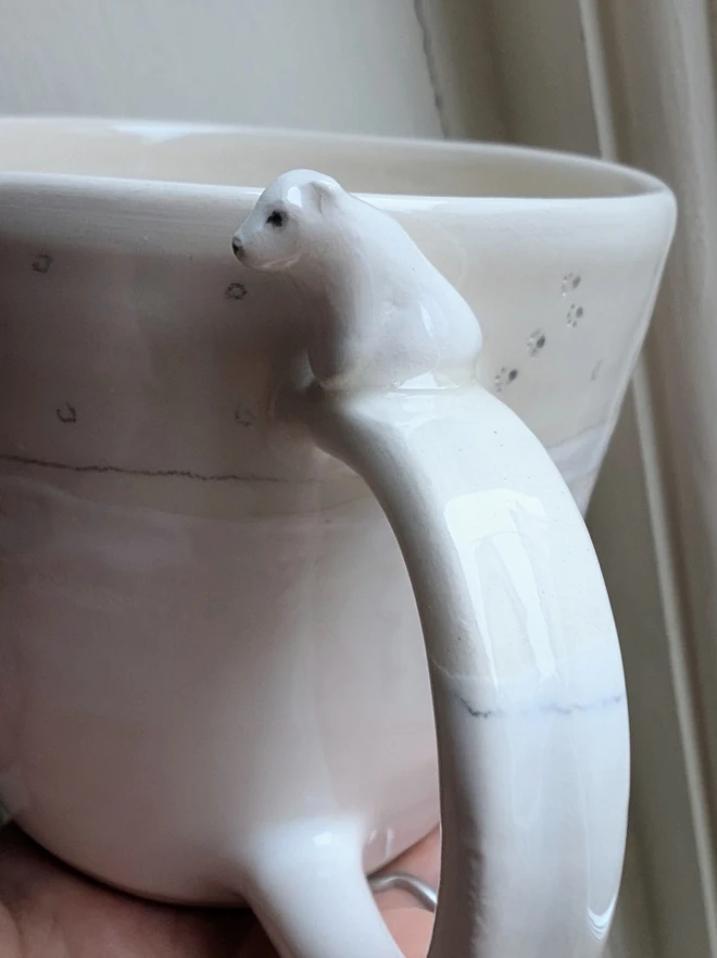 white cup with a close up of a ceramic polar bear sitting on the handle with tiny paw prints on the cup