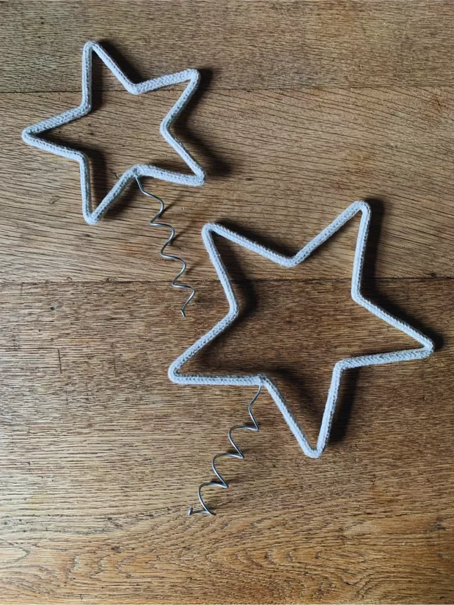 A small and a large string covered wire star with a coil for topping a Christmas tree on an oak table