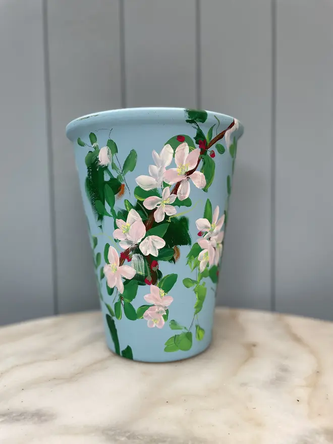 Unique hand-painted terracotta pot featuring apple blossoms on a pale blue background