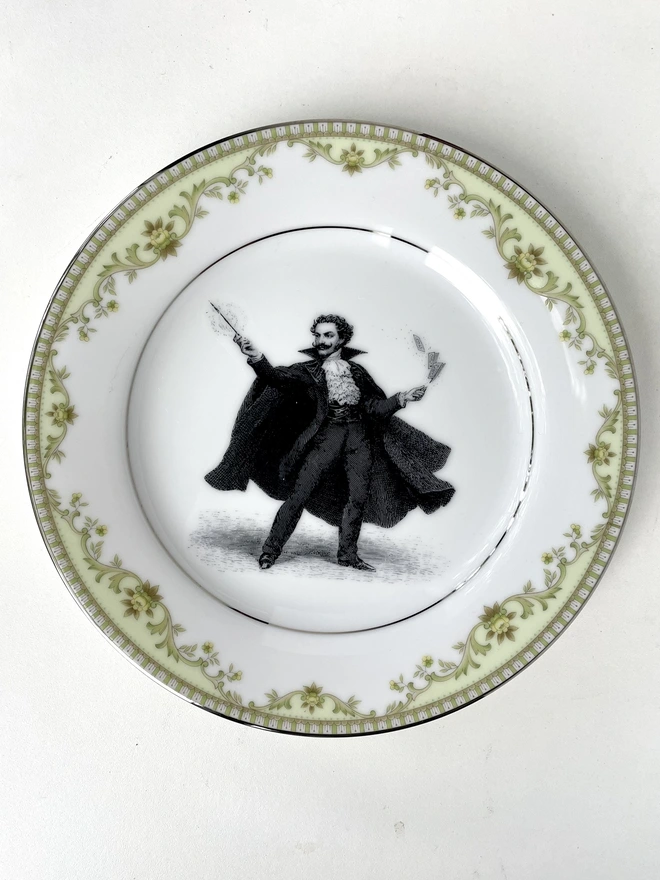 a vintage ornate plate in the centre i have printed a vintage black and white illustration of a dramatic magician cape wearing moustache casting spells with his wand