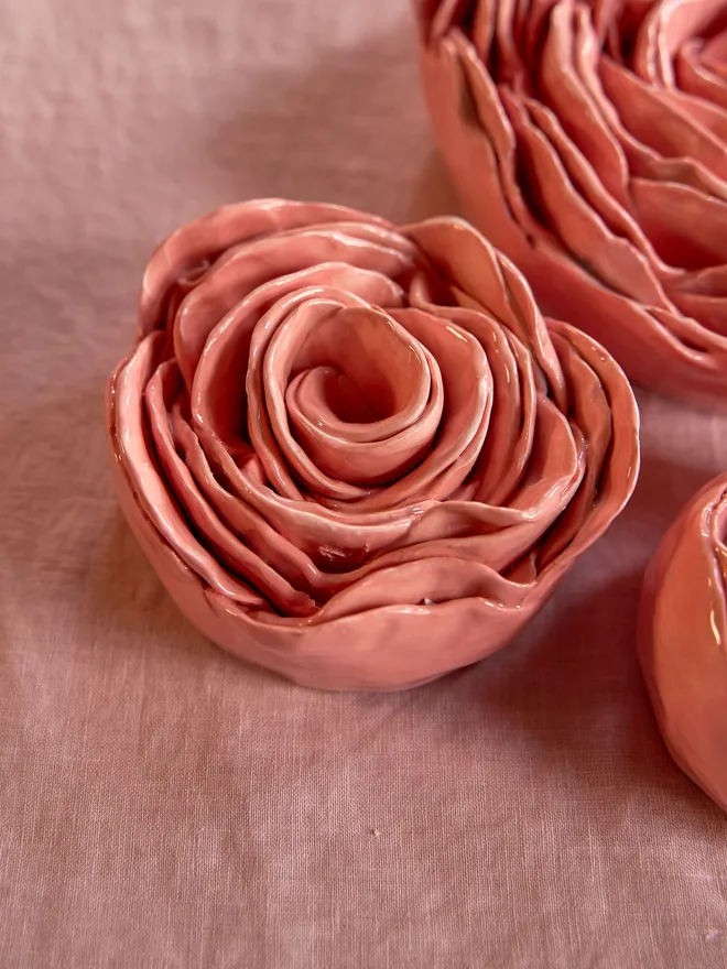 Medium sized ceramic rose on a pale pink tablecloth surrounded by two other ceramic roses