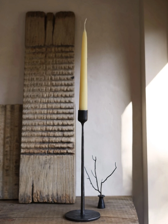 Forged Steel Candle Stick, a metal candle stick sitting on a wooden surface against a wood backdrop. 