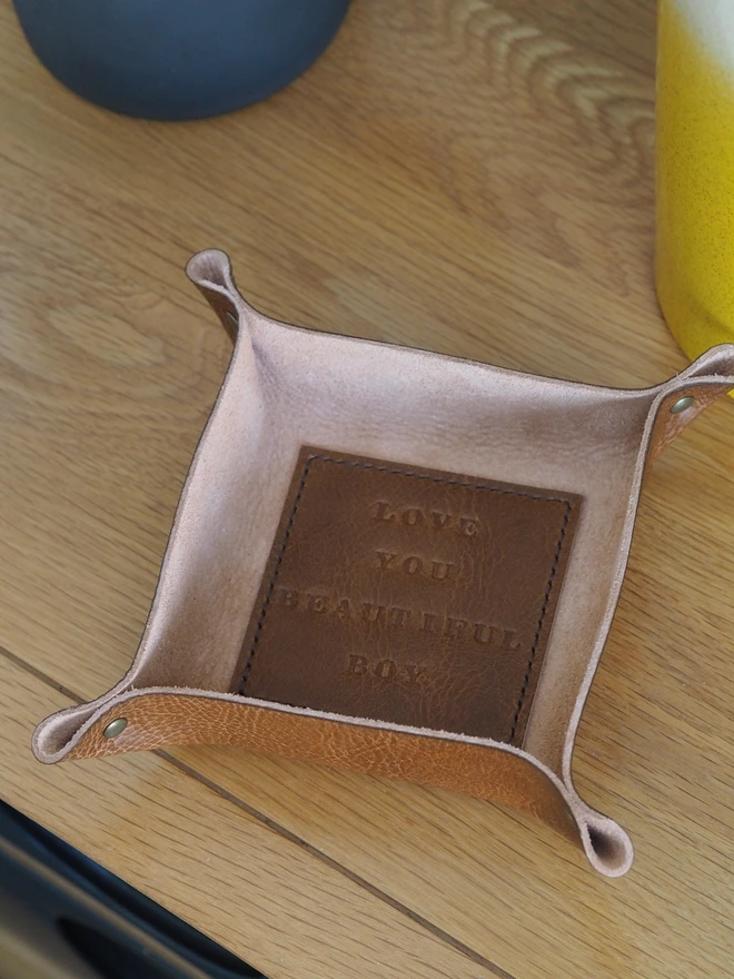 Personalised message leather coin tray. Hand dyed tan brown leather tray with a square stitched to the base which is personalised with a short but sweet message.