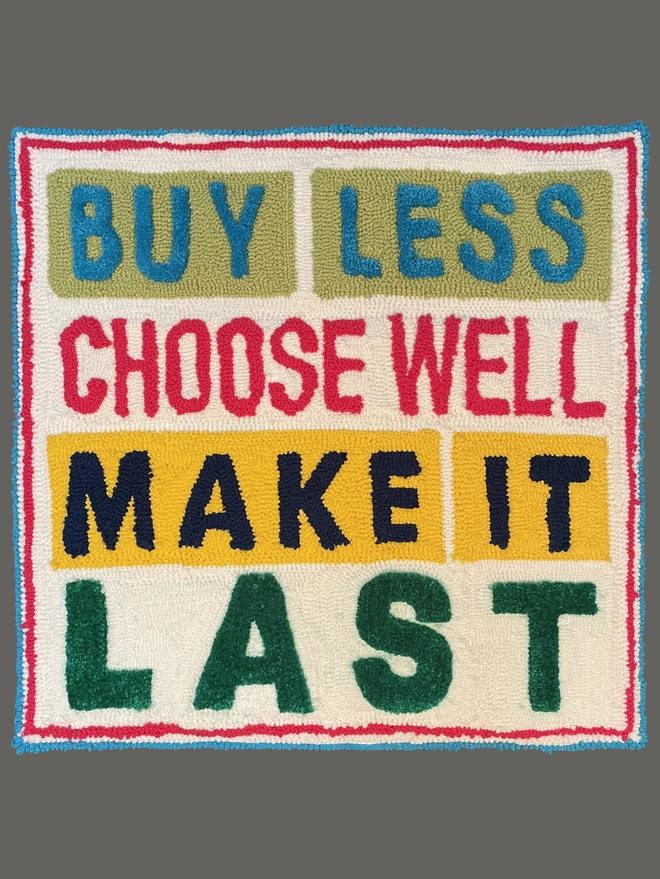 Vivienne Westwood's quote of "buy less, choose well,  make it last" written in bold uppercase letting in tufted wool on a square cream backing with blue and red square tufted frame