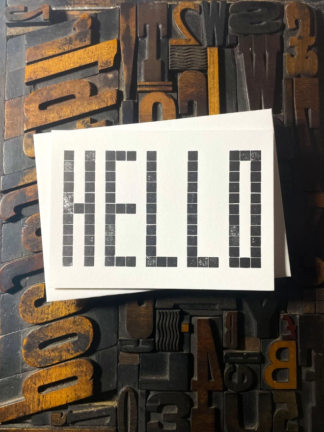 Letterpress HELLO postcard printed from a grid of square wooden type blocks in rich black ink, deeply impressed on thick 350gsm Colorplan Pristine White card.