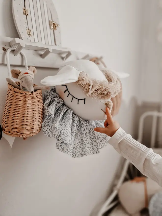 Sheep Head Wall Mount, a hanging sheep head decoration sitting against a plain wall in child's bedroom. 