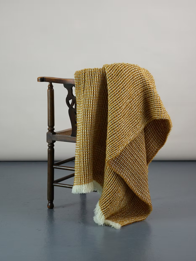Grainne Honeycomb Lambswool Blanket. a yellow textured blanket photographed thrown over a chair.