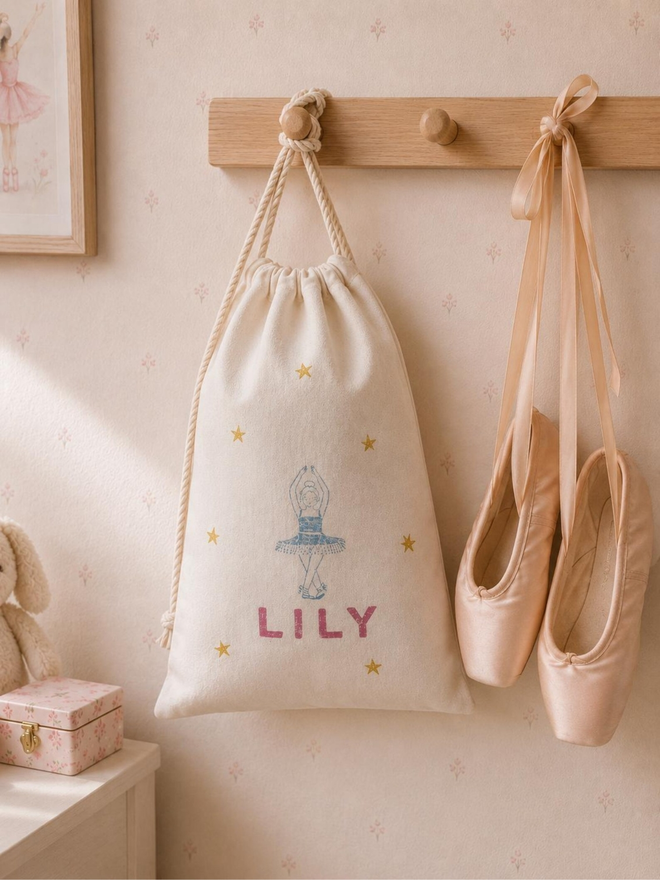 personalised ballet bag. a drawstring ballet bag with a personalised name hanging up next to ballet shoes.