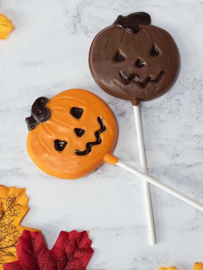 Orange and milk chocolate pumpkin lollipops surrounded by leaves