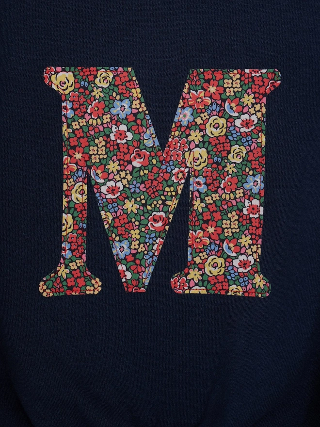 a kids navy sweatshirt with the initial M personalised in floral liberty print on the front, close up of appliqué stitching