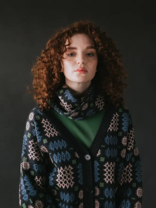 Model wearing pieces from MABLI's 'Carthen' collection, featuring the Carthen Cardigan in the vibrant 'Emeralds' colour-way. The design showcases bold, colourful patterns inspired by traditional Welsh blanket tapestry.