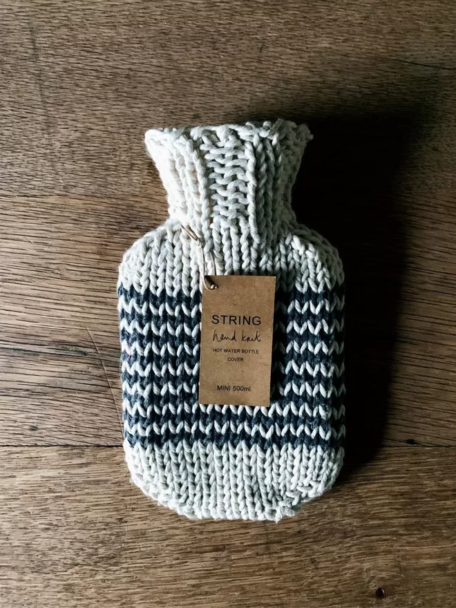 Mini Hot Water Bottle in hand knit string cover with black stripe on an oak table