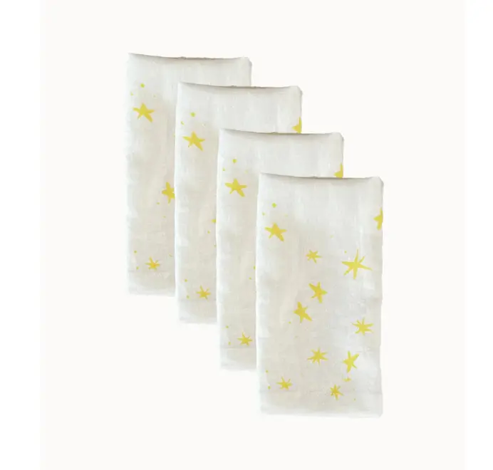 Stars Napkins In White (Set of 4). Set of four white cloth napkins with scattered yellow star prints, stacked in a staggered arrangement.