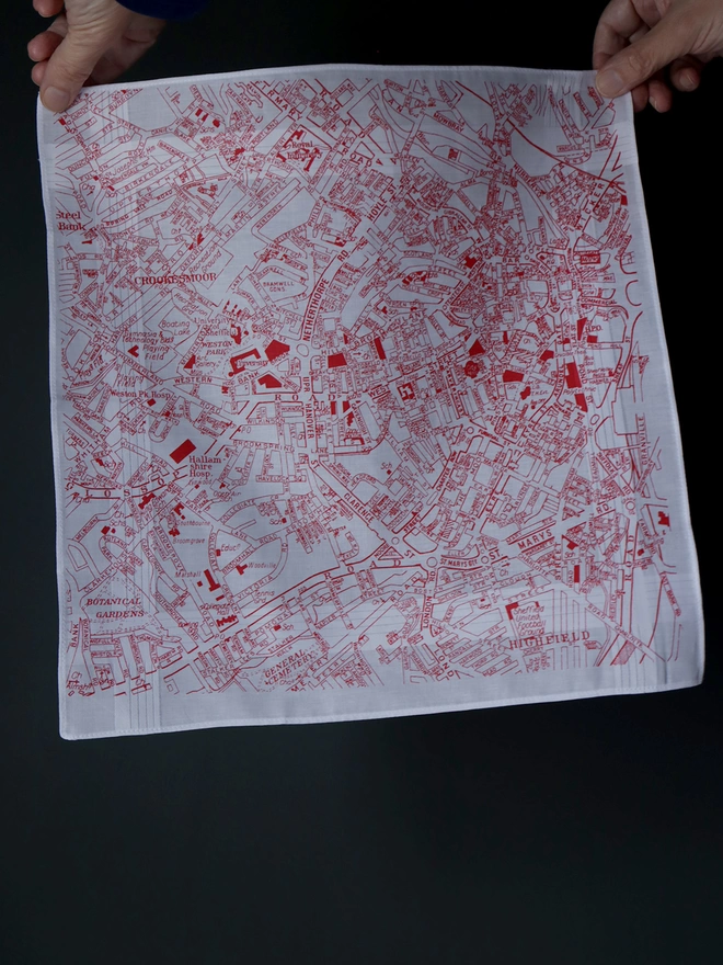A Mr.PS Sheffield map hankie printed in red held aloft in front of a dark wall