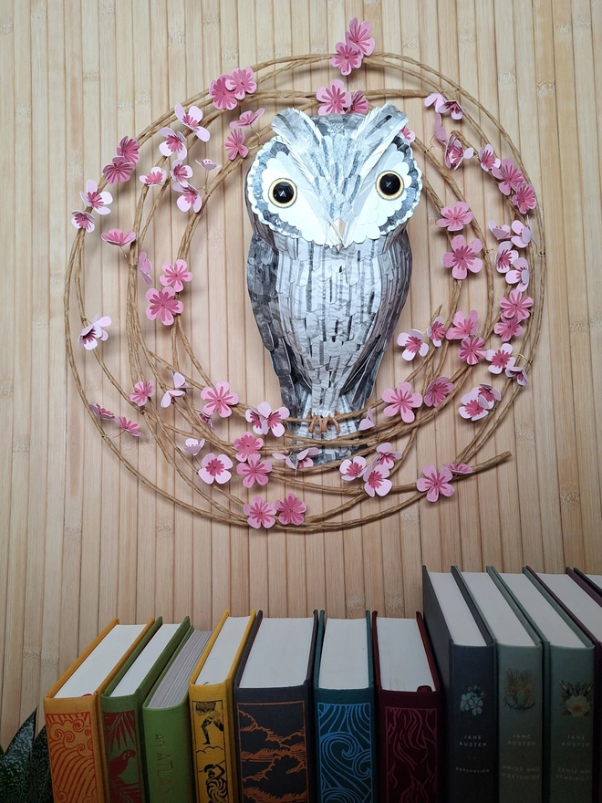 Handmade sculpture of a grey owl perched on a floral wreath of pink blooms