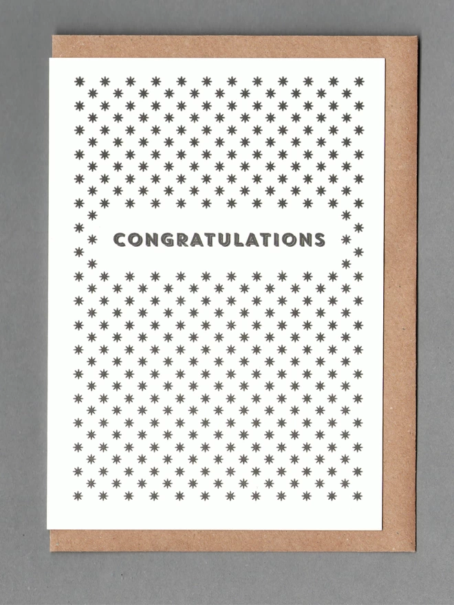 White card with black stars and black text reading 'CONGRATULATIONS' with a kraft envelope behind it