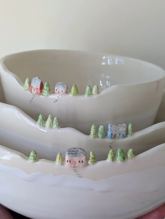 A nesting trio of Handmade ceramic white bowls with a tiny village of houses and tree details on the rim and white glaze 