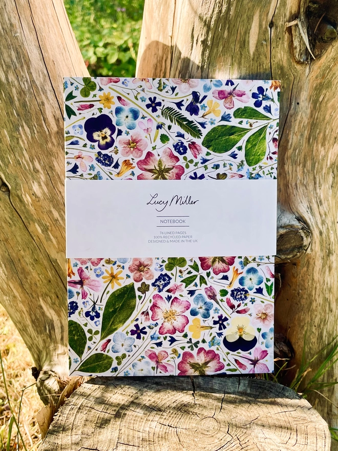 Nature-Inspired Notebook with Pressed Flower Design Cover, 'Lucy Miller' Branded Belly Band, Leaning Against Tree Trunk