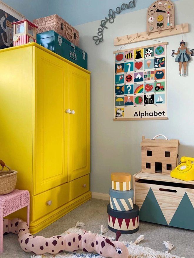 illustrated alphabet wall print in a childs bedroom with yellow wardrobe and toys