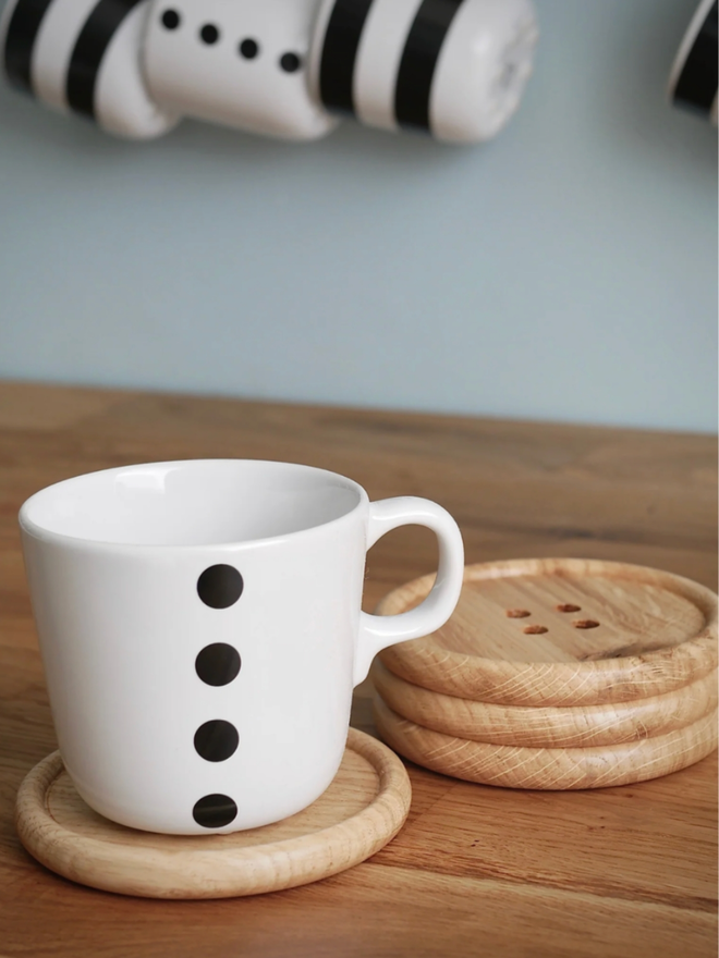 Wooden Button Drink Coaster. A stack of three button coasters. A fourth is nearby with a mug placed on it.
