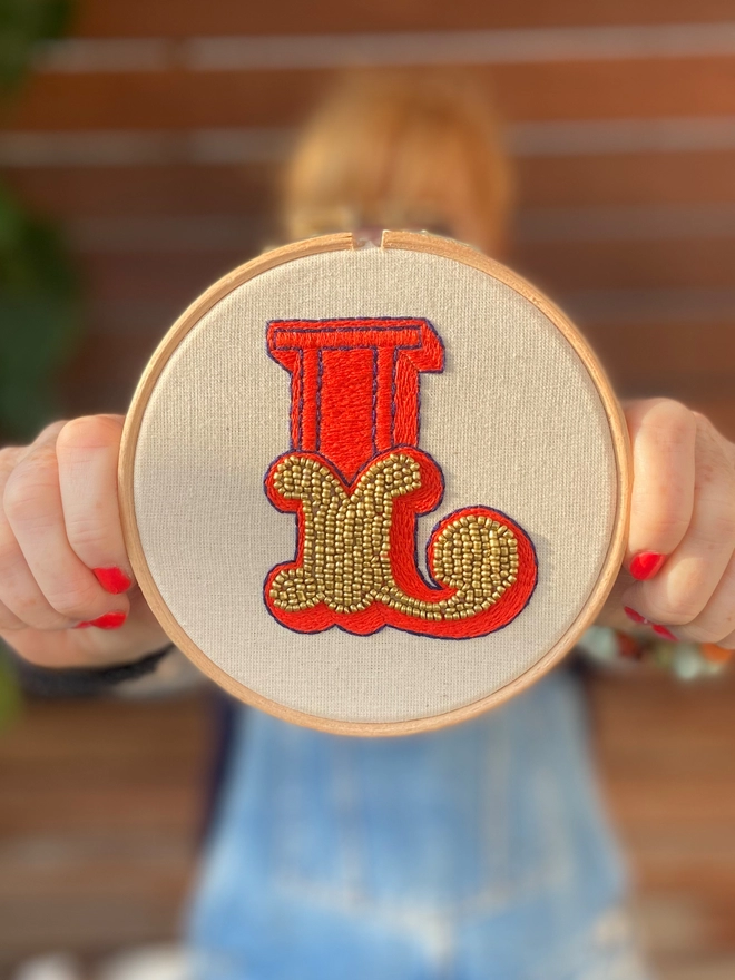 An embroidered letter L in a hoop being held out in front of a female