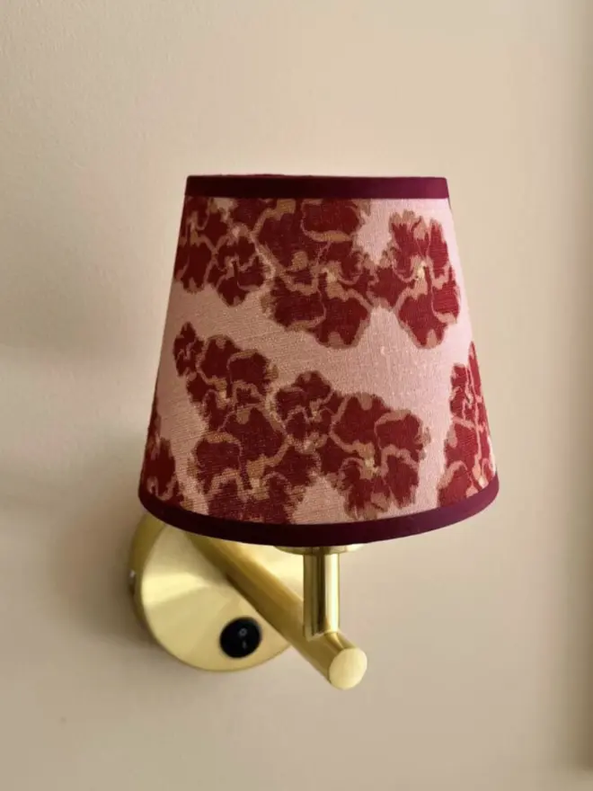 Rose coloured Ronko lampshade affixed to golden wall sconce