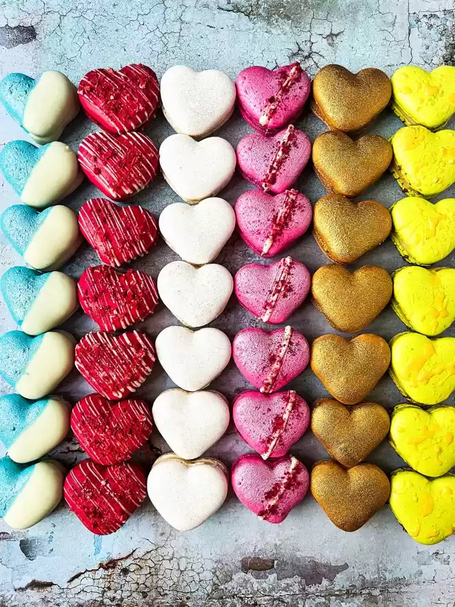 a row of colourful heart shaped macarons on a blue background
