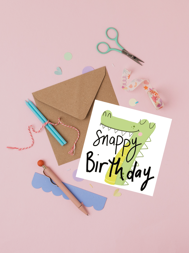 'snappy' illustrated 7th birthday card. card featuring green crocodile shaped like a number 7.