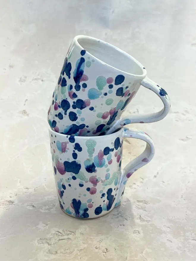 Sweetpea Standard Mug, a pair of colourful mugs stacked on top of each other on a stone surface. 
