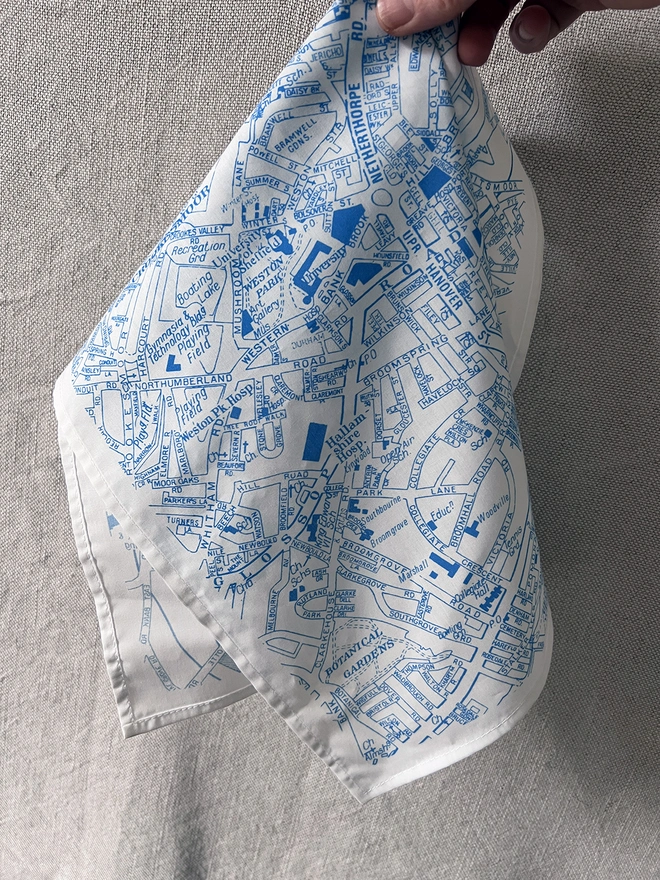 A white hand holds a Mr.PS Sheffield Handkerchief in front of a linen curtain