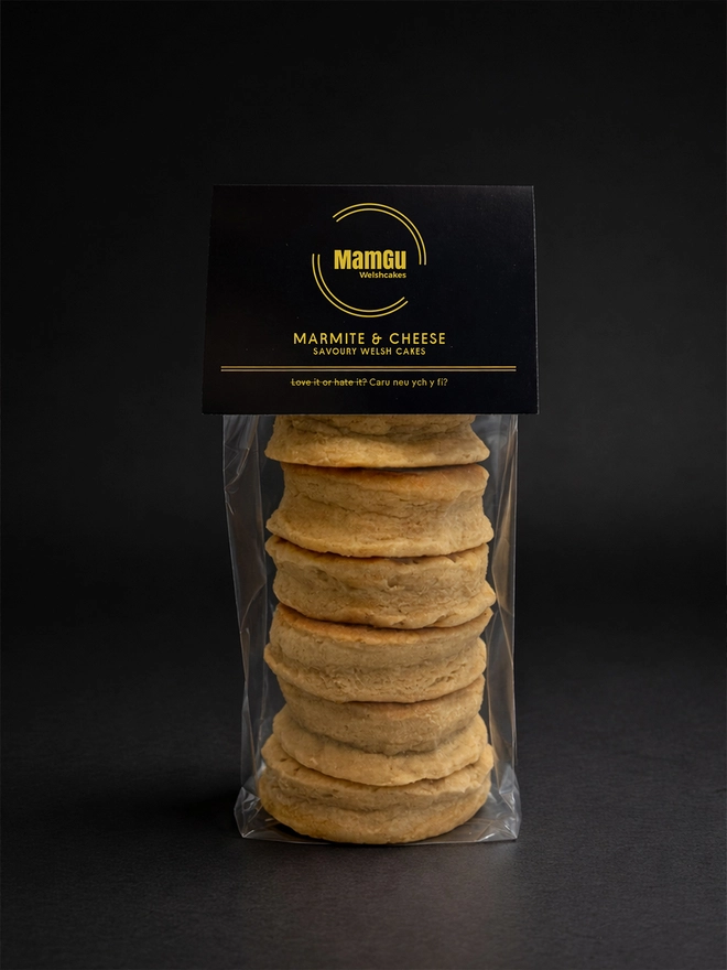 6 marmite and cheese welsh cakes stacked in packaging with a black MamGu label and black studio background