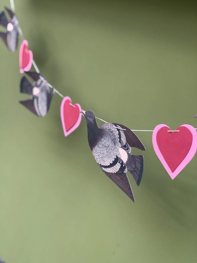 a paper garland of pigeons and hearts against a green wall