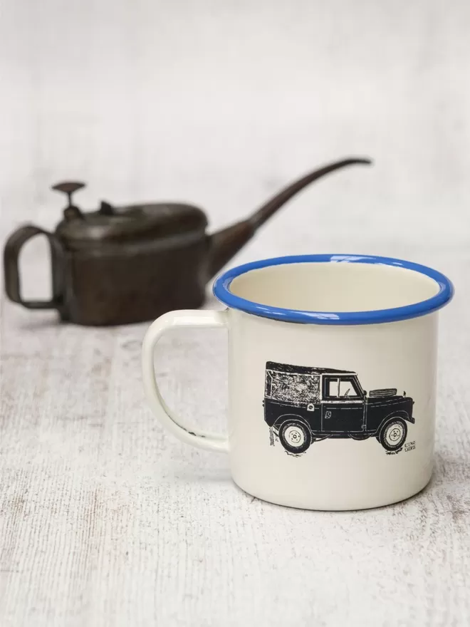 Picture of a Cream Enamel Mug with a Blue Rim with a Land Rover design etched onto it, taken from an original Lino Print