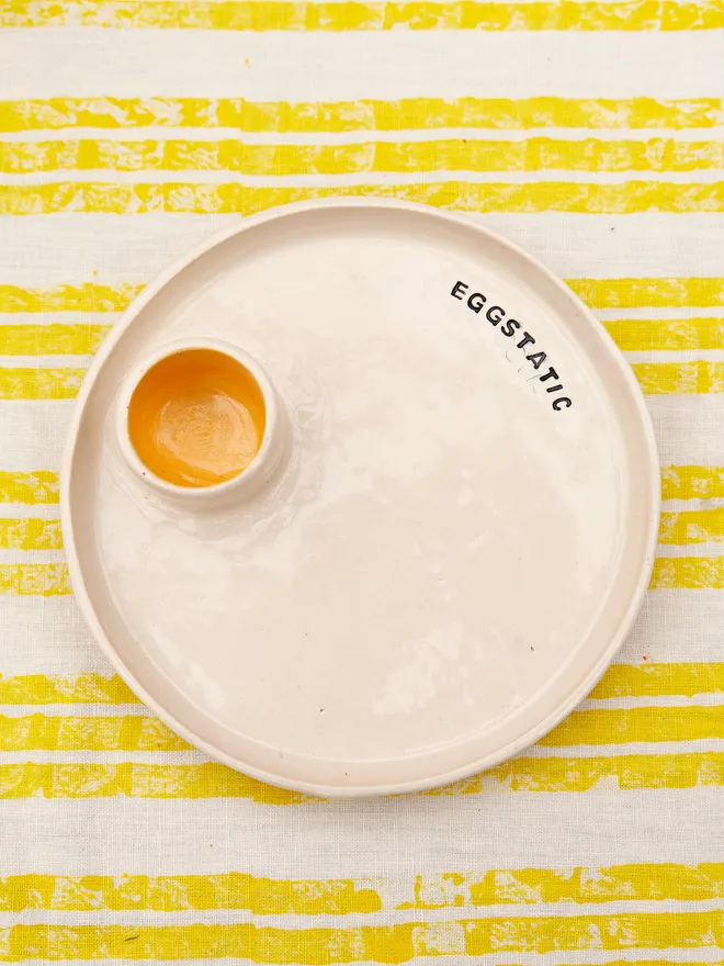 Egg And Soldier Plates, a plate with an integrated egg cup placed on a yellow striped surface. The wording reads 'eggtastic' 